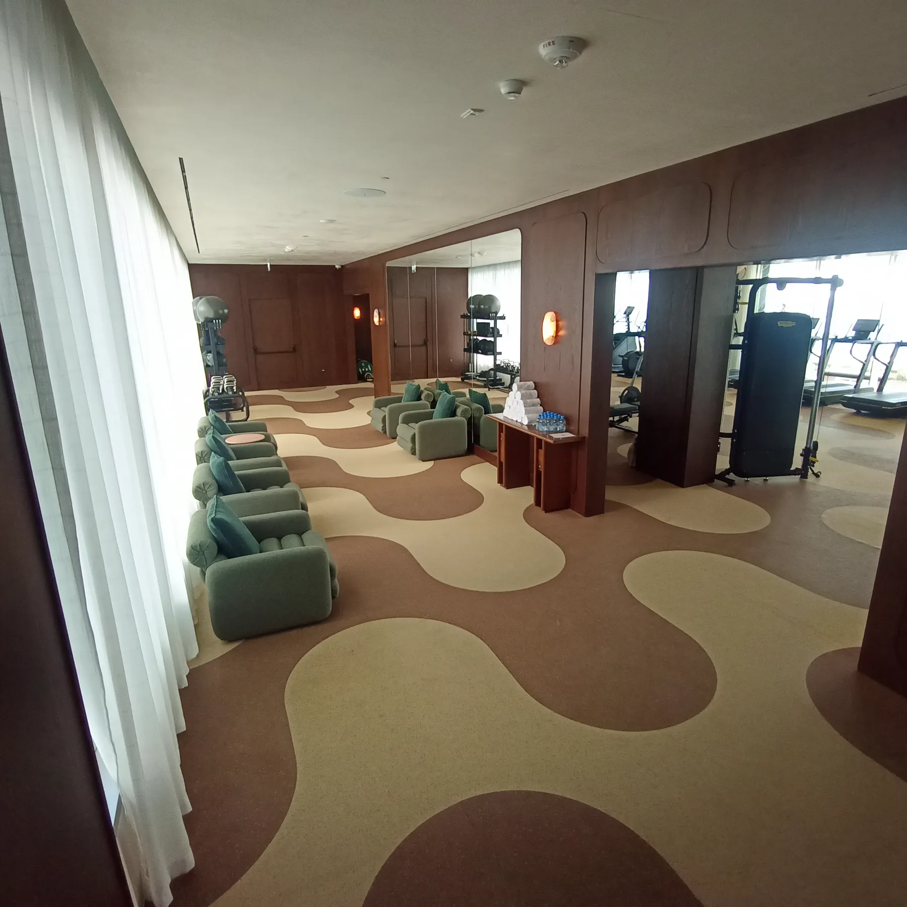 Row of sage armchairs on a bespoke two-tone carpet in a Doha hotel wellness lounge with floor-to-ceiling curtains