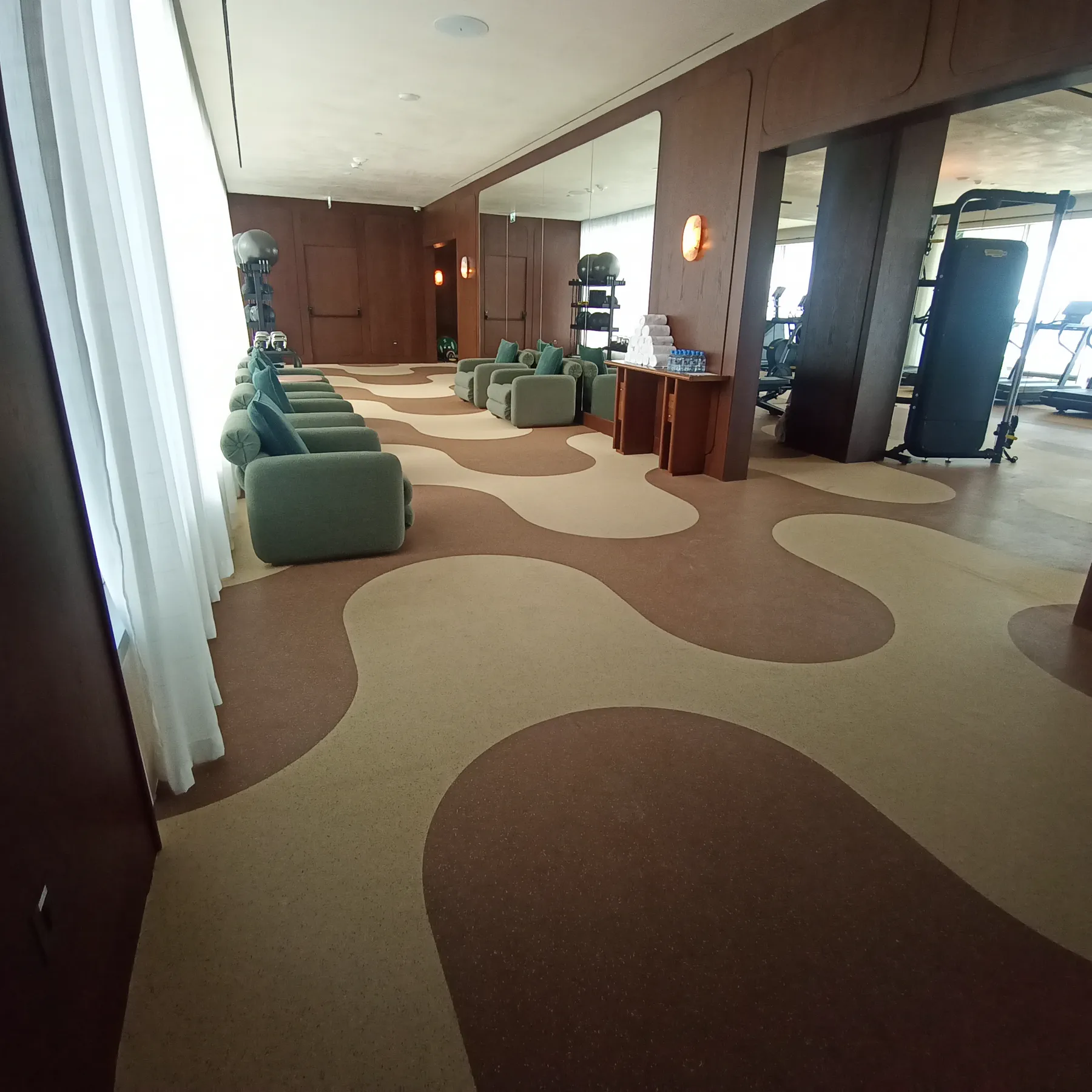 Hotel wellness lounge in Doha with a custom-cut carpet floor in flowing sand and taupe shapes, sage armchairs and timber panelling