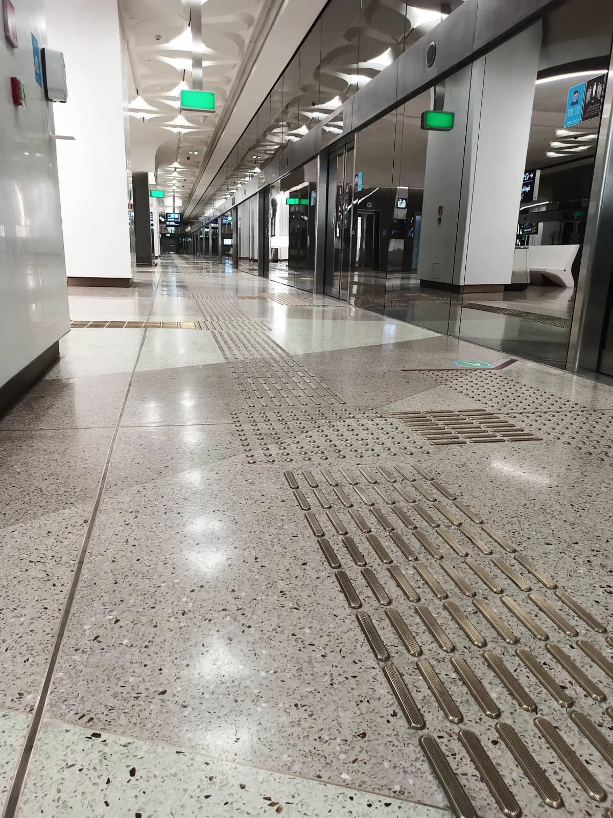 Polished terrazzo platform floor at a Doha Metro station with brass tactile guidance strips leading along the platform edge