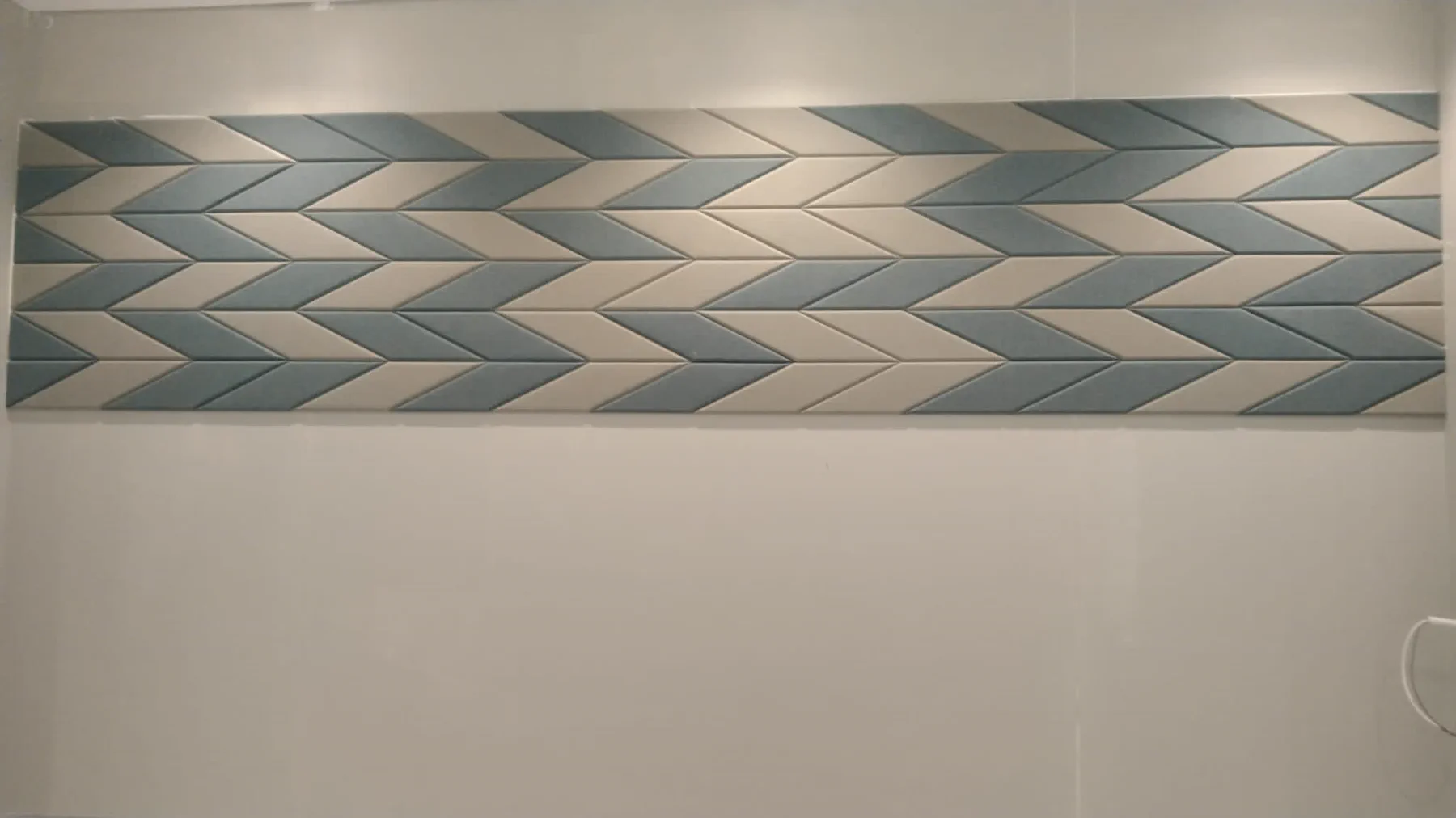 Completed fabric-wrapped acoustic panel installation on a plain white wall, showing the teal and cream chevron layout made by KTS in Doha