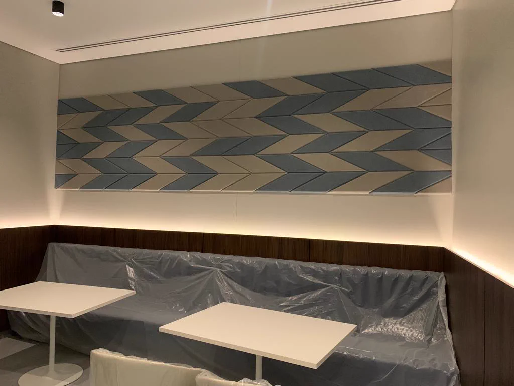 Close view of a fabric-wrapped chevron acoustic panel array in blue and sand tones mounted above timber wall panelling in a Doha library café