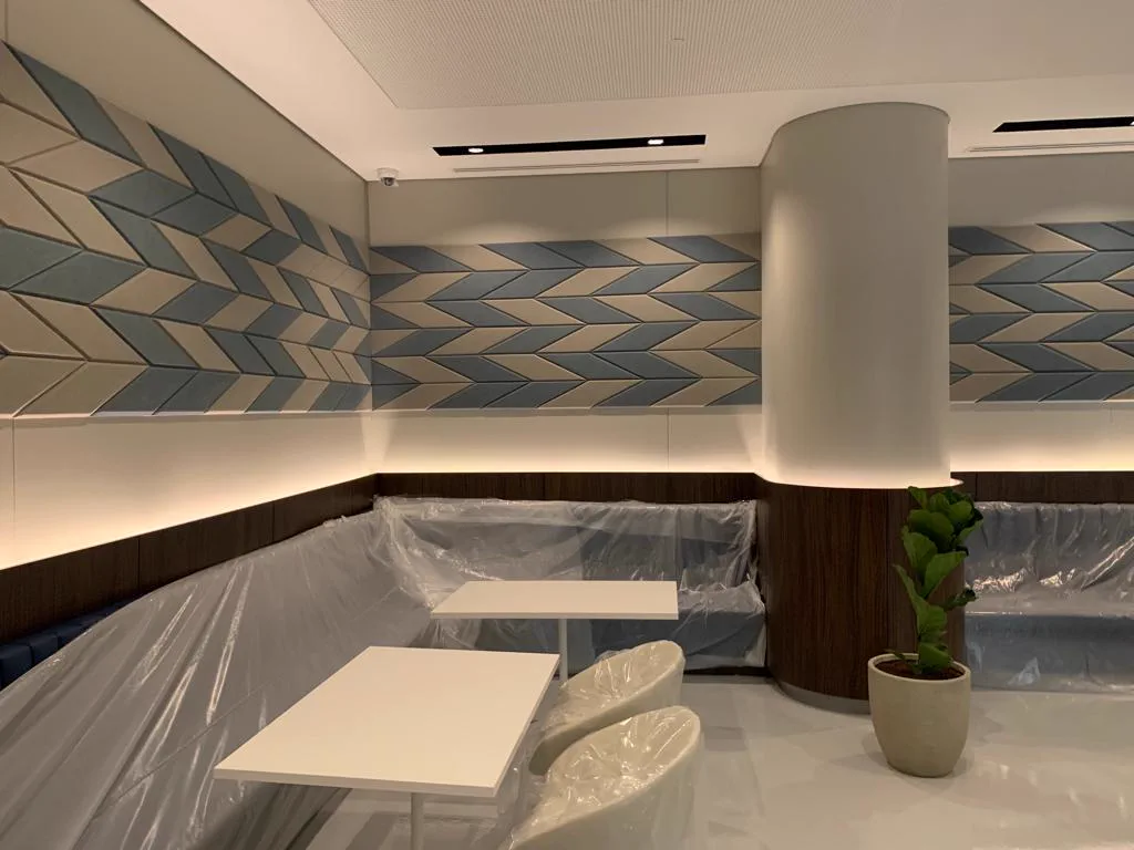 Fabric-wrapped acoustic panels wrapping two walls of a library lounge in Doha, Qatar, with cove lighting and a curved column