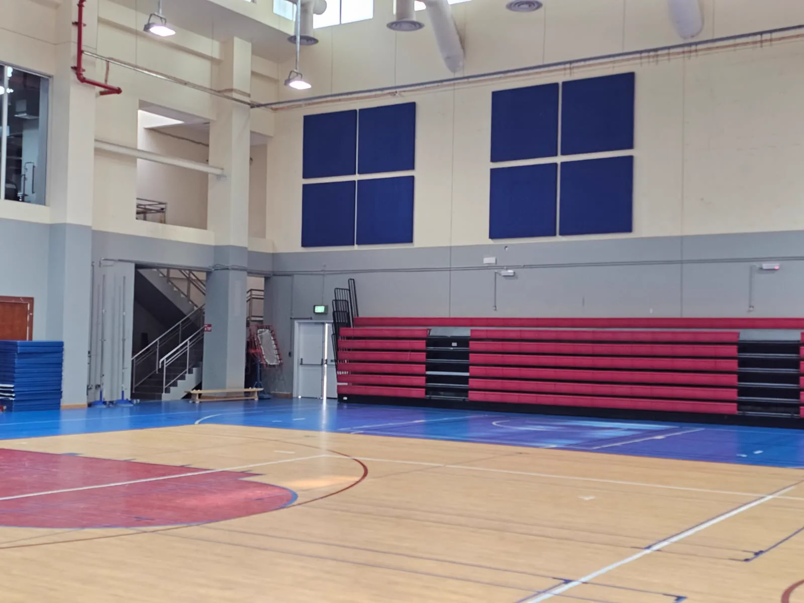 Navy blue acoustic wall panels mounted above red retractable bleachers in a school gymnasium in Doha, Qatar