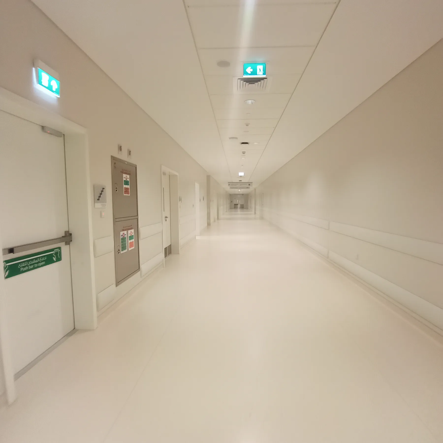 Long hospital corridor in Doha with seamless welded vinyl sheet flooring, coved skirting and illuminated emergency signage