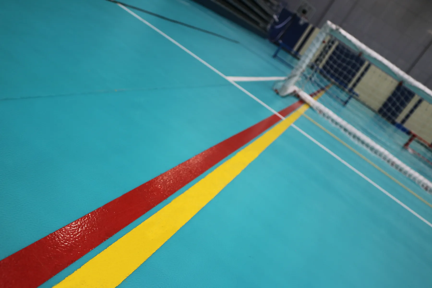 Close detail of red, yellow and white court line markings on turquoise indoor sports flooring at a Doha school