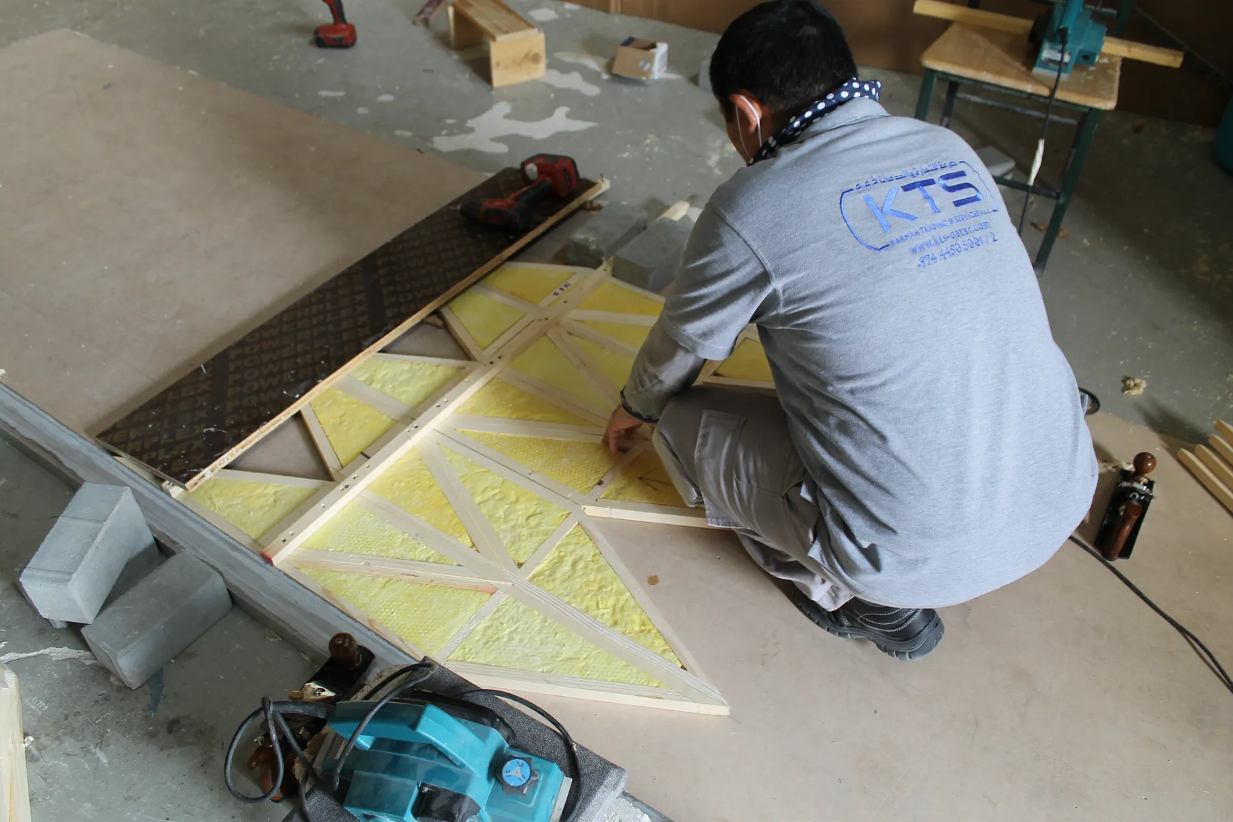 Yellow fibreglass acoustic cores being laid into chevron-shaped panel frames by a KTS technician in Doha, Qatar