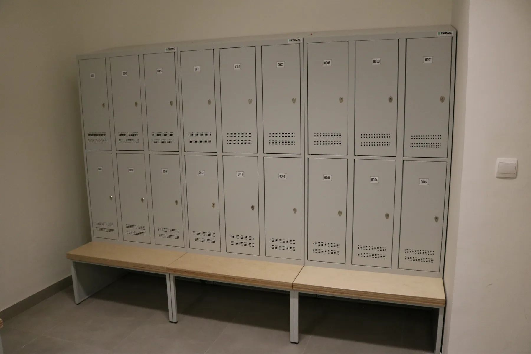 Two-tier grey metal lockers above a timber-topped changing bench in a staff changing room in Qatar