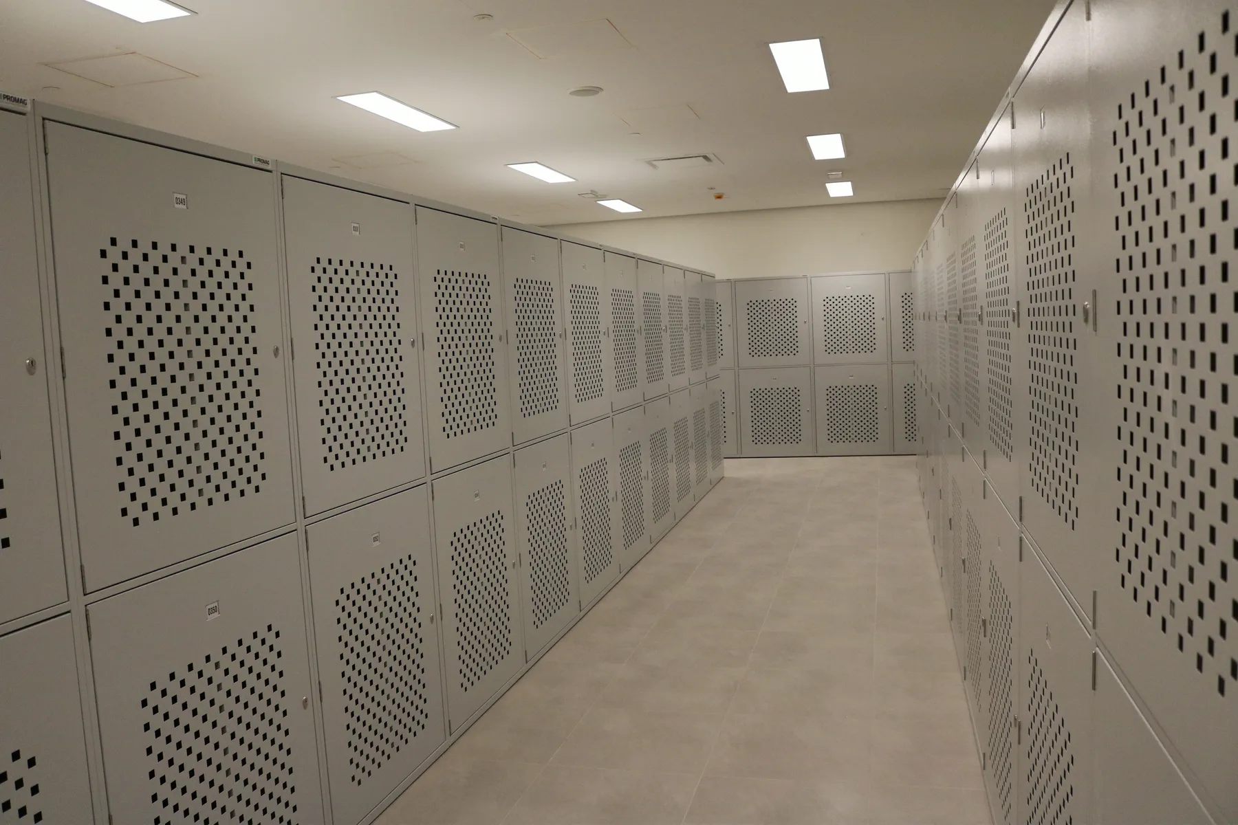 Rows of tall grey perforated metal lockers lining both sides of a changing room corridor at a naval base in Qatar