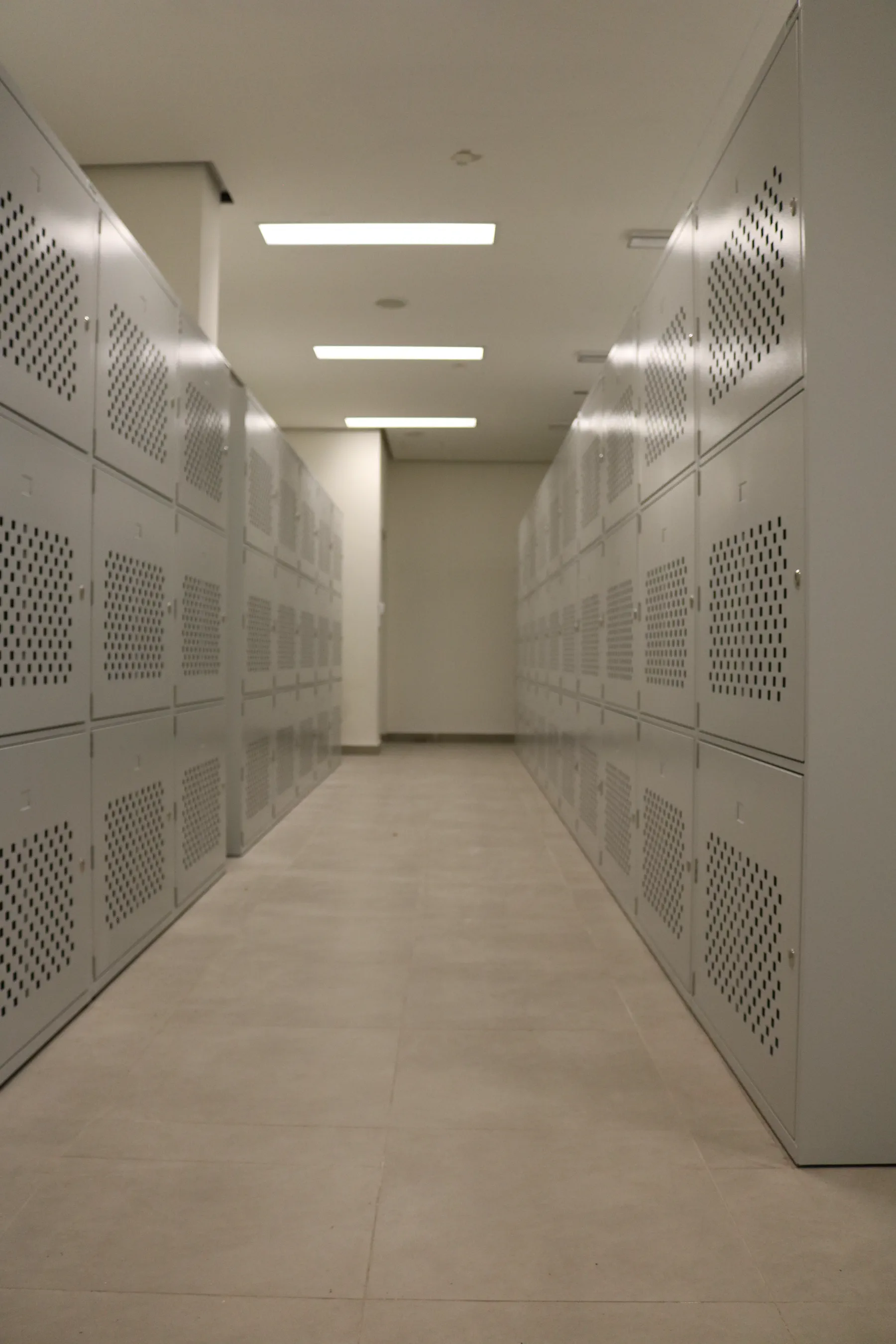 Ventilated metal locker corridor with perforated doors and linear ceiling lighting at a naval base facility in Qatar