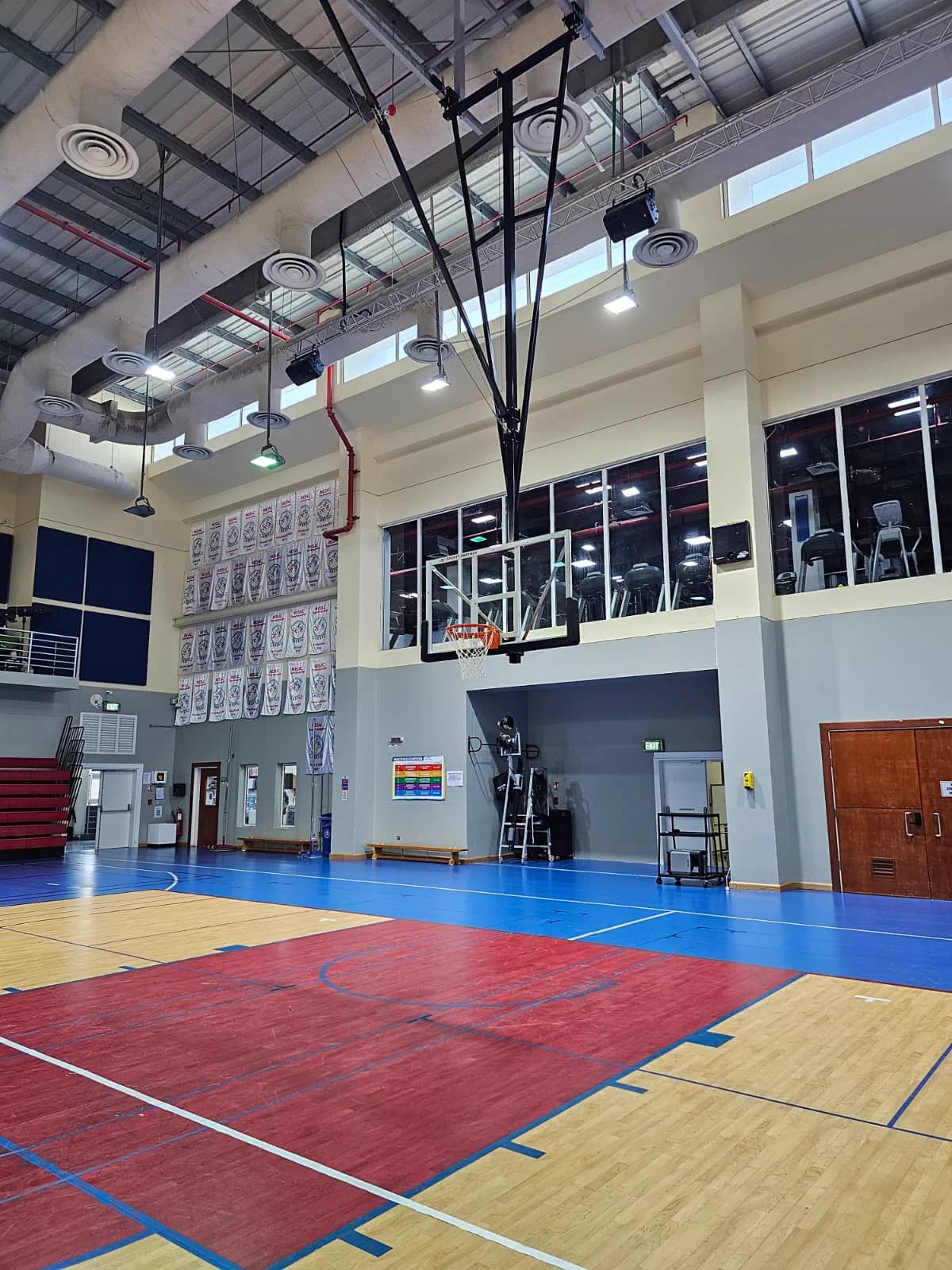 Ceiling-suspended retractable basketball backstop lowered over a maple court in a school gymnasium in Doha, Qatar