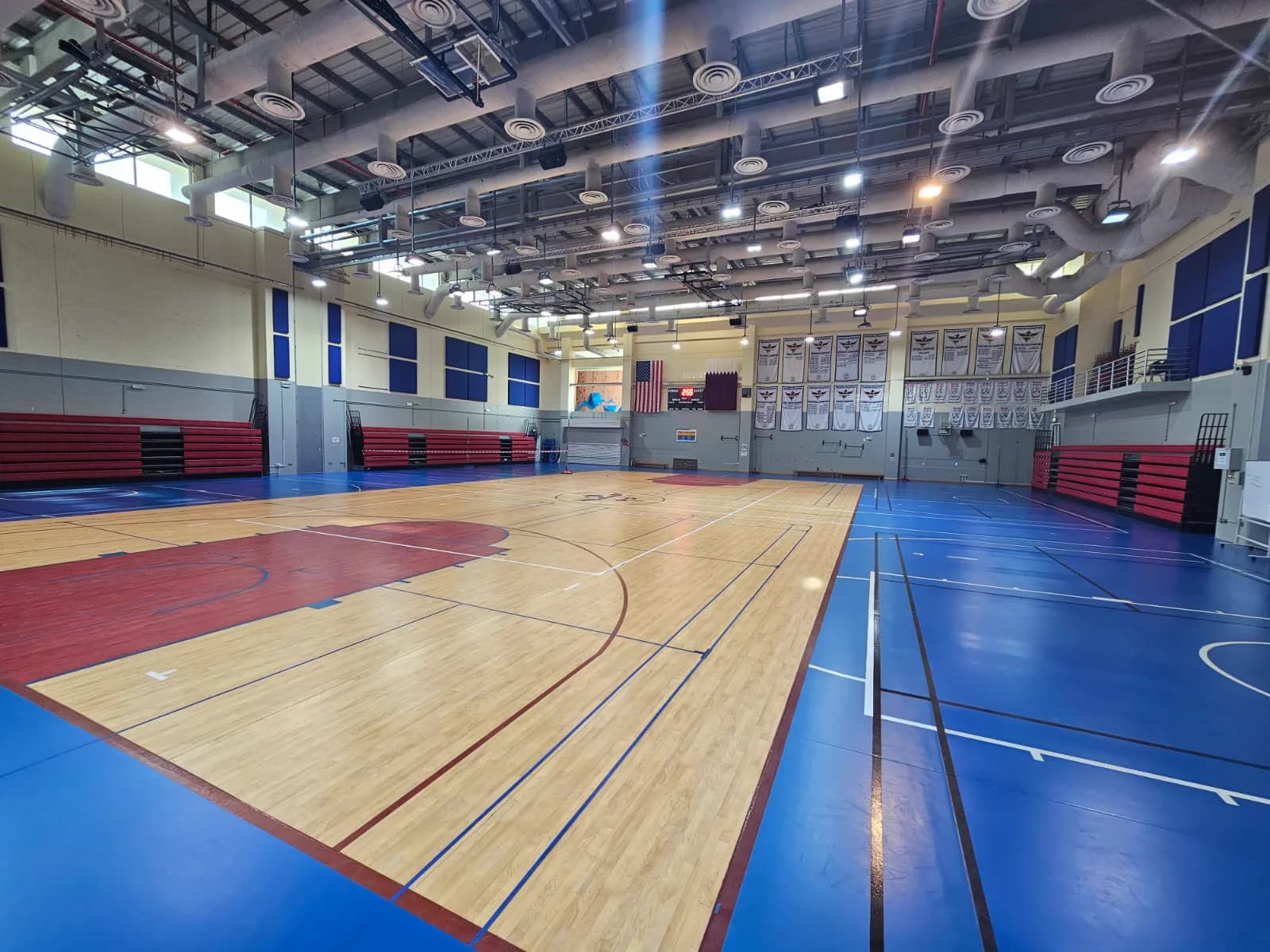 School gymnasium in Doha combining a maple timber basketball court with blue and red synthetic sports flooring and red retractable bleachers