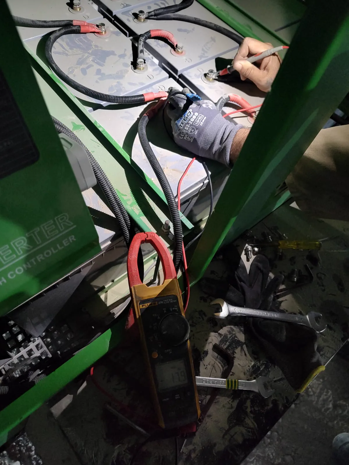 Technician testing battery terminals and charge controller wiring inside a KTS mobile solar tower light cabinet
