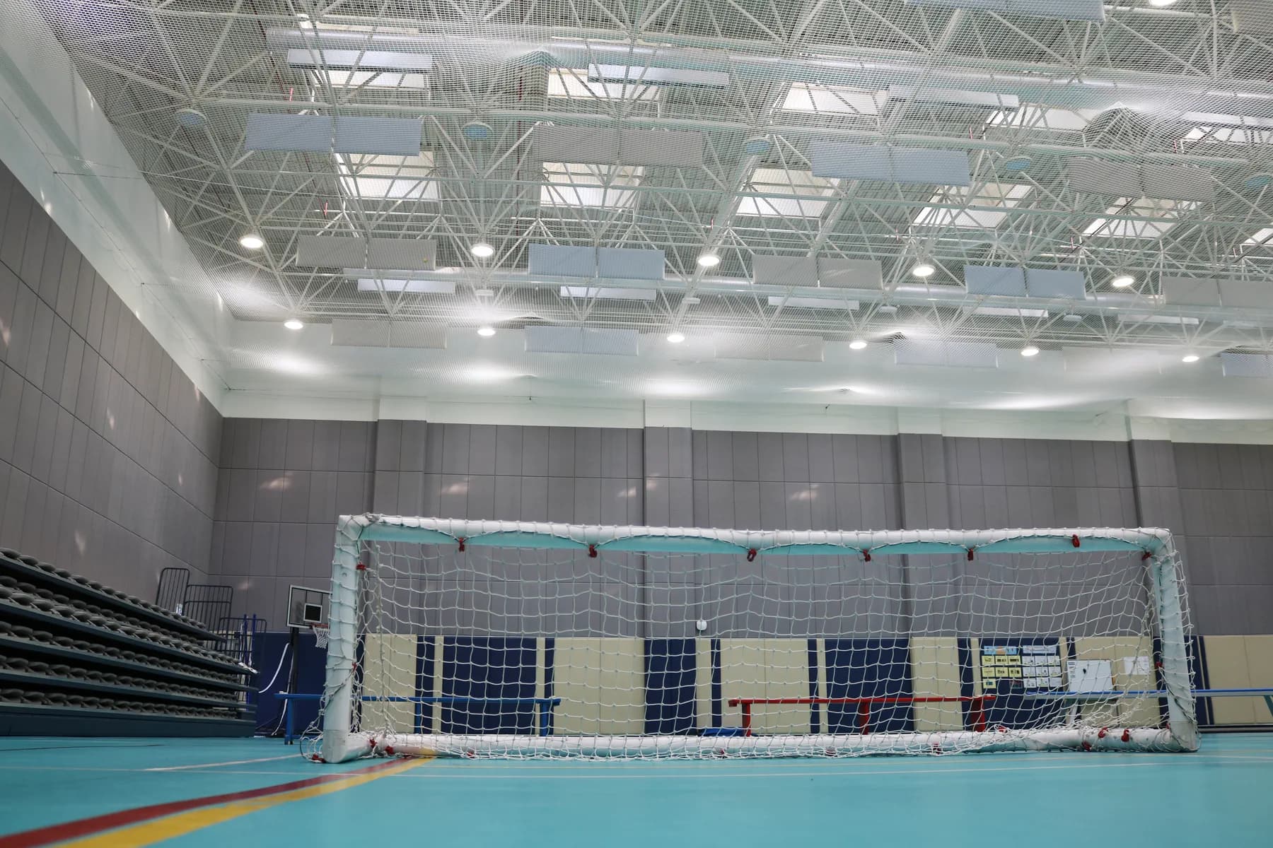 Handball goal on turquoise sports flooring in front of full-height grey acoustic wall panels in a Doha school sports hall