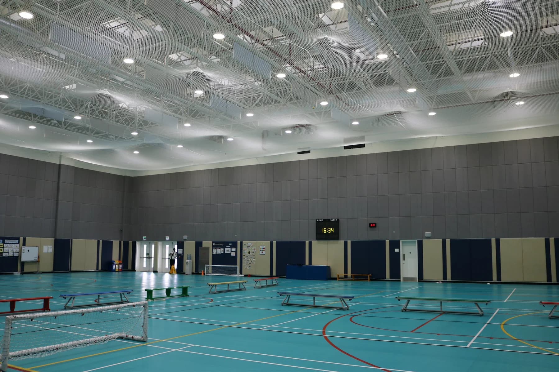 Wide view of a double-height school sports hall in Doha with grey acoustic panels covering the upper walls and an exposed steel roof structure