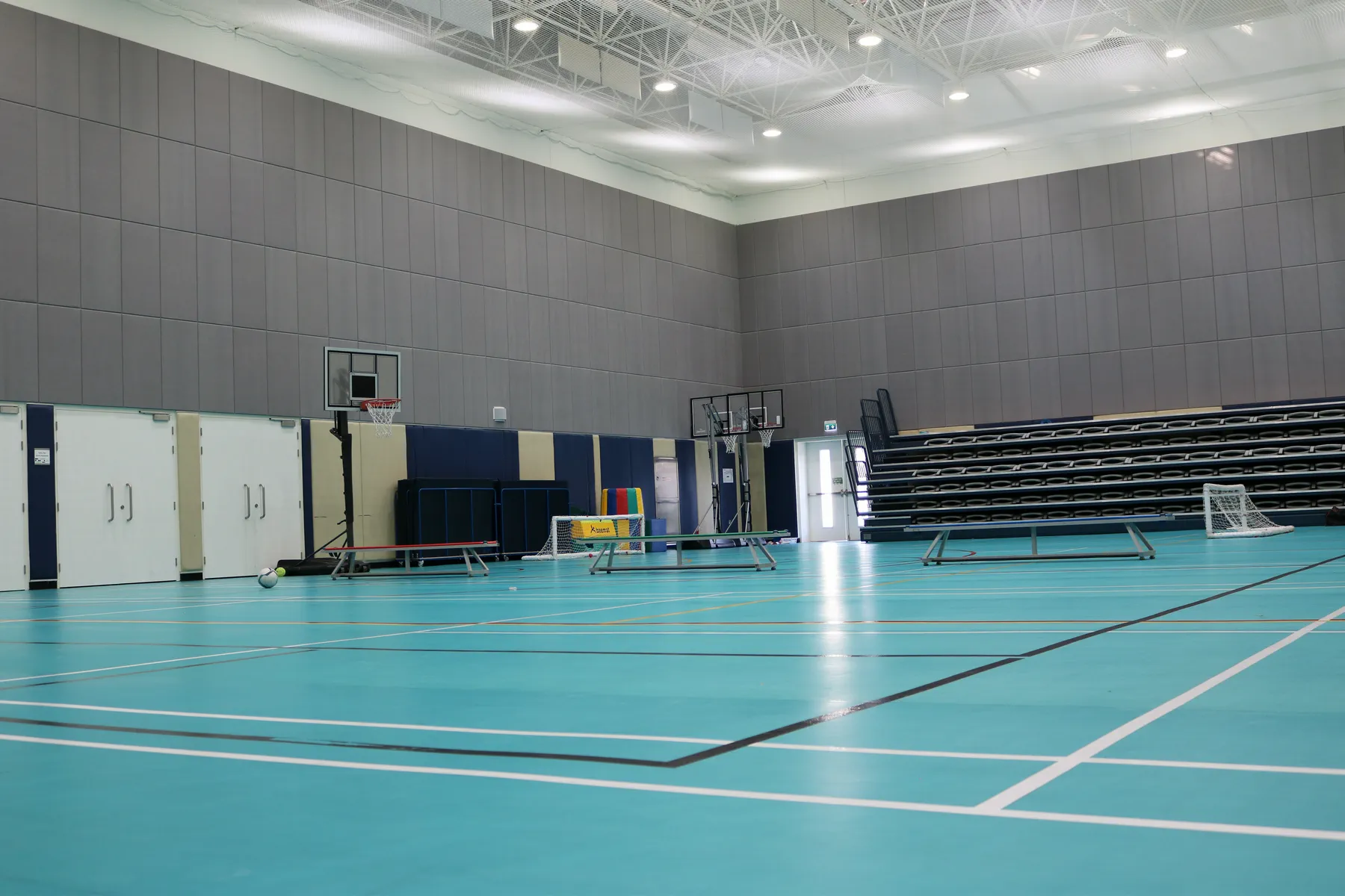 School sports hall in Doha with grey acoustic wall panels, turquoise seamless sports flooring and retractable bleacher seating