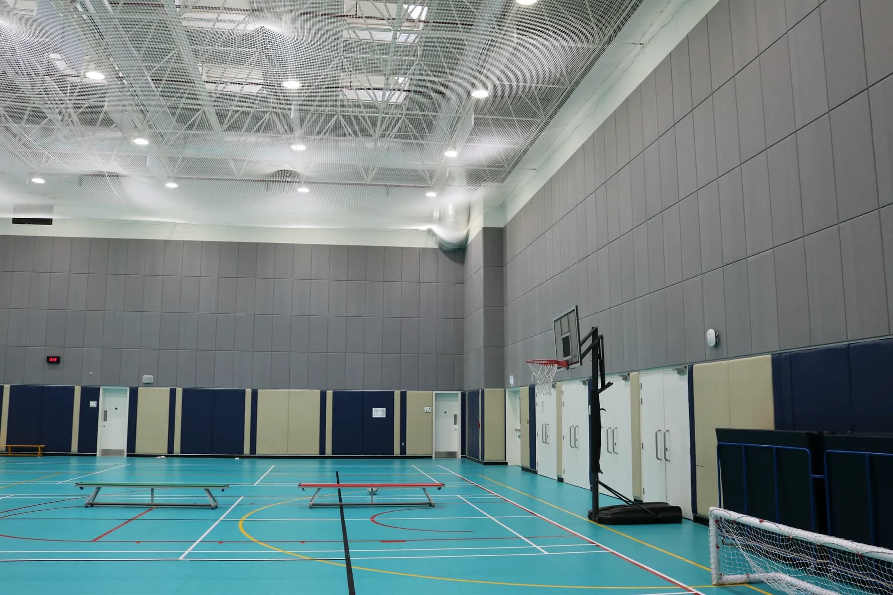 Portable basketball system and retractable bleachers in a Doha school sports hall lined with grey acoustic wall panels