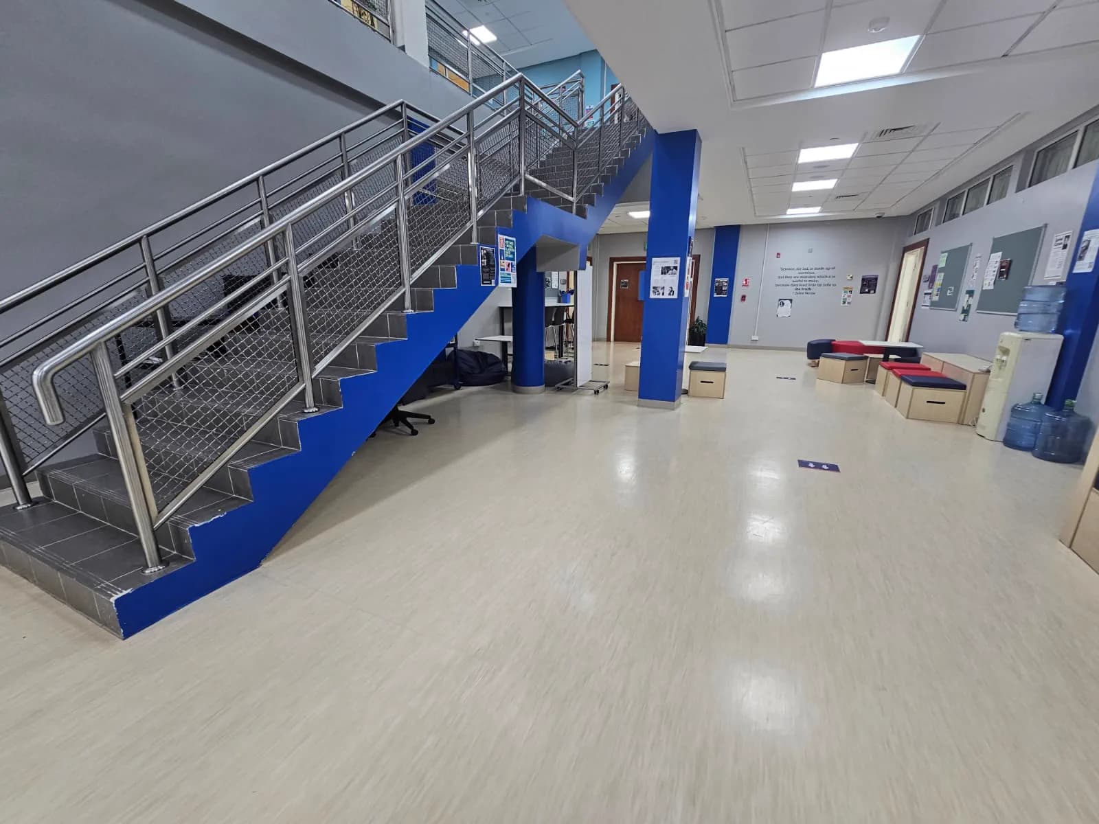 Bright school lobby in Doha with light vinyl sheet flooring, a blue-clad stairwell and stainless steel balustrade